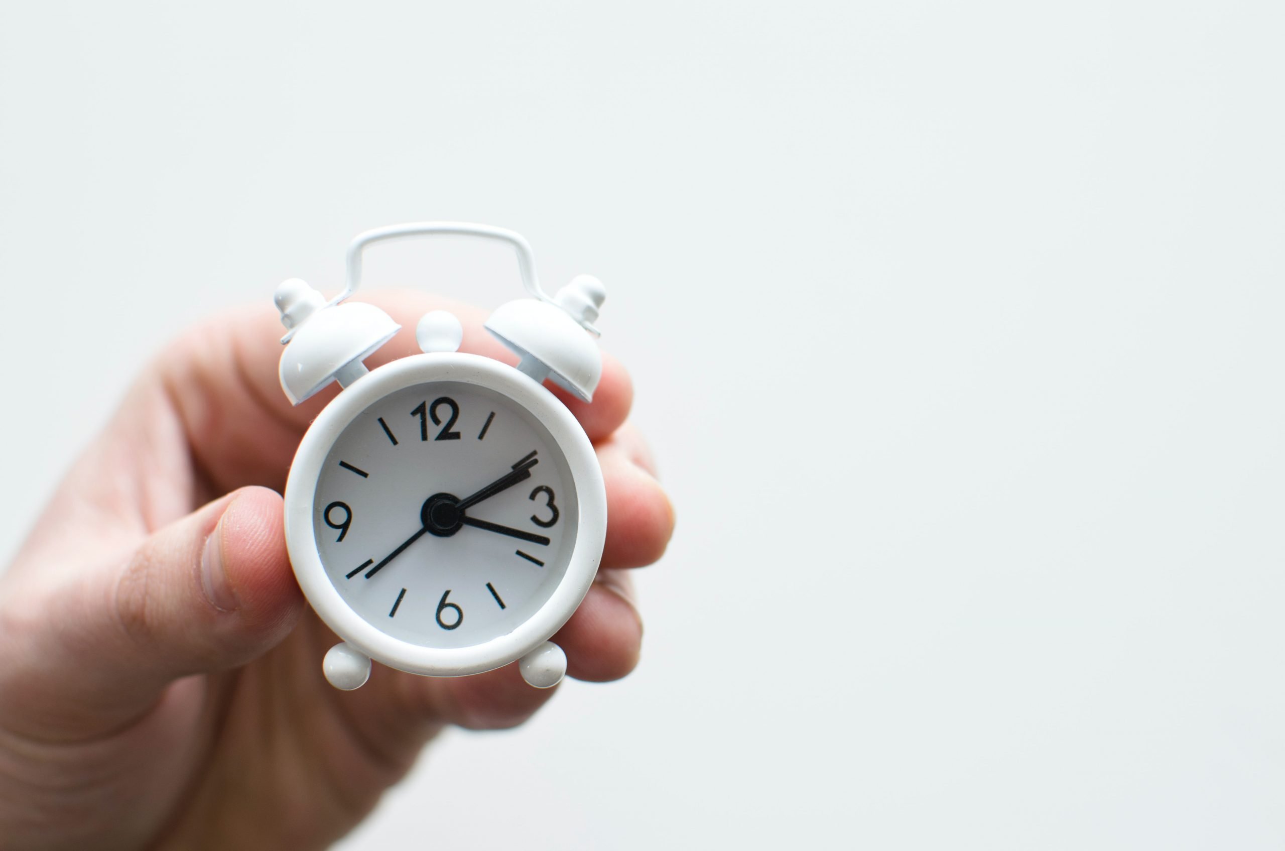 Hand holding small white alarm clock